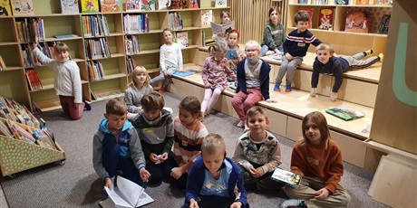 Powiększ grafikę: Na zdjęciu widać dzieci z klasy 1b, które siedzą na dywanie w bibliotece i czytają książki.