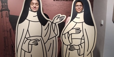Powiększ grafikę: uczennice z twarzami w otworach stojaka przedstawiającego zakonnice - norbertanki