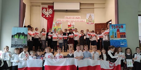Powiększ grafikę: Uczniowie stoją na scenie i pod sceną z biało - czerwonymi flagami i sercami.